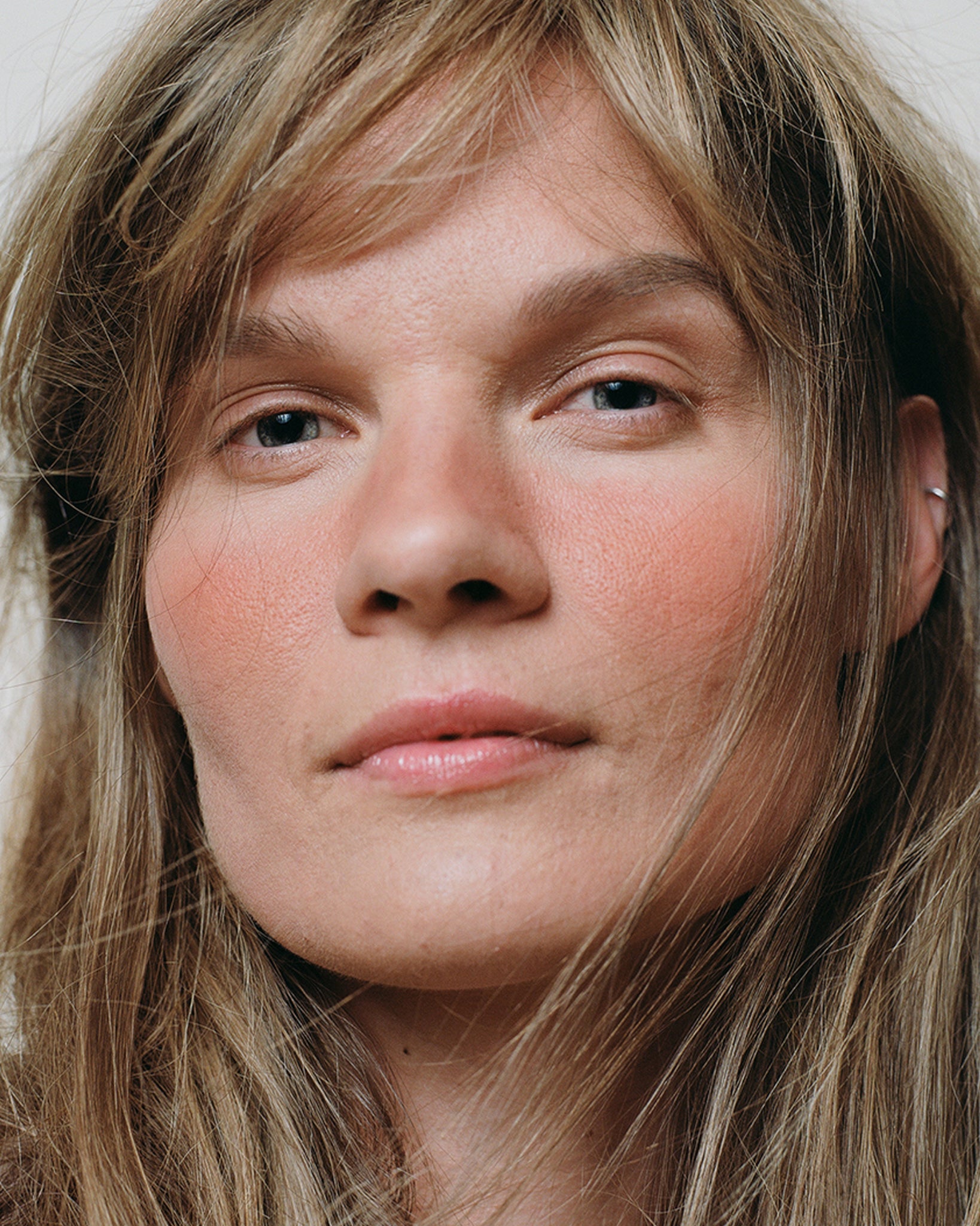 Model wearing MΓDARA Organic Skincare mineral cheek blush fierce flame on A6821 on skin; close-up portrait shows natural application results.